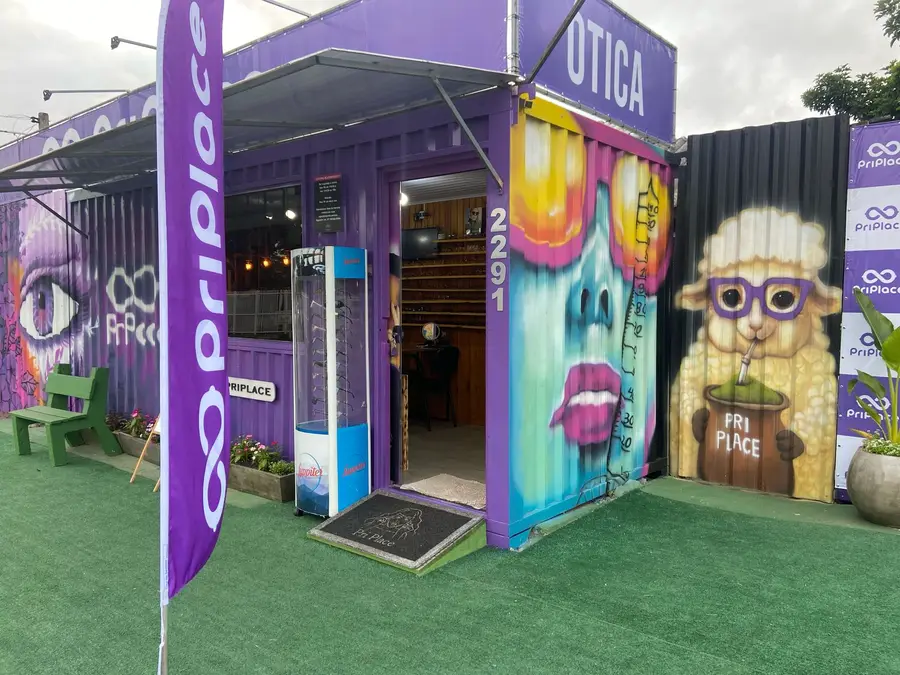 Fachada da Pri Place: container roxo com grafites coloridos, bandeira e grama na frente