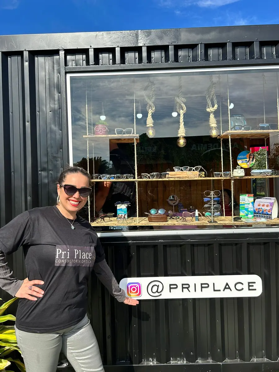 Pri em frente à vitrine da loja, com prateleiras de madeira cheias de armações